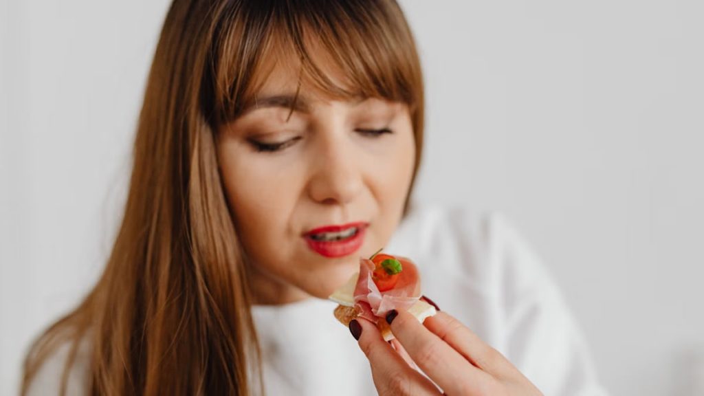 Woman with long hair savoring a gourmet canape indoors.